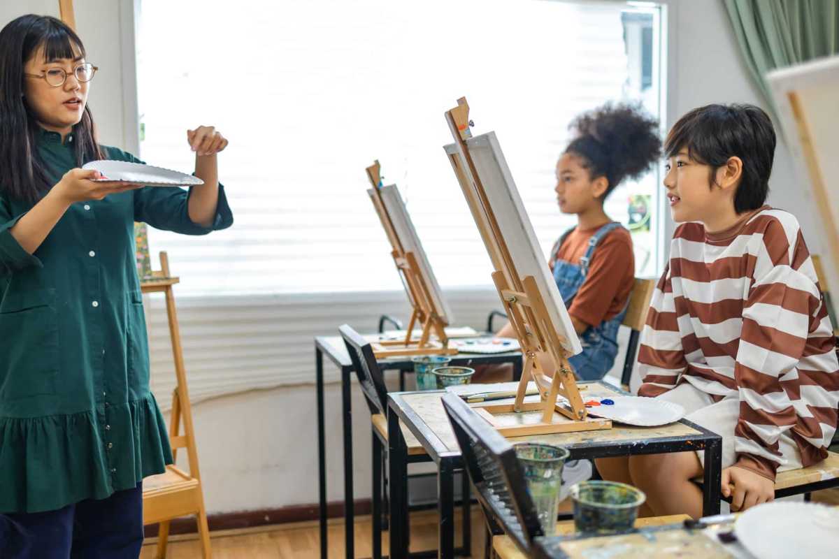 African and asian  kid drawing in classroom, young girl happy funny study and play painting acrylic color on canvas.Group of  children drawing with  teacher in school studio.