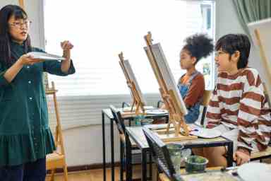 African and asian  kid drawing in classroom, young girl happy funny study and play painting acrylic color on canvas.Group of  children drawing with  teacher in school studio.