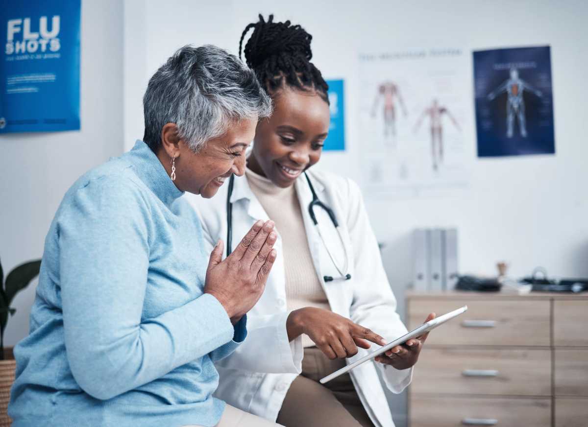 Black woman, doctor and senior patient with tablet, results and happy for health clearance, advice or report. African medic, mobile touchscreen and healthcare with smile, tech and support in hospital