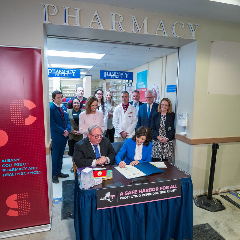 a group of people at a table as Kathy Hochul signs standing order about hormonal contraceptives