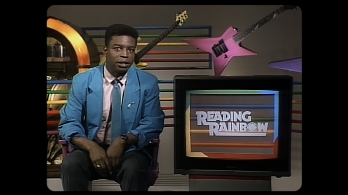 actor LeVar Burton from Reading Rainbow sitting down next to a TV