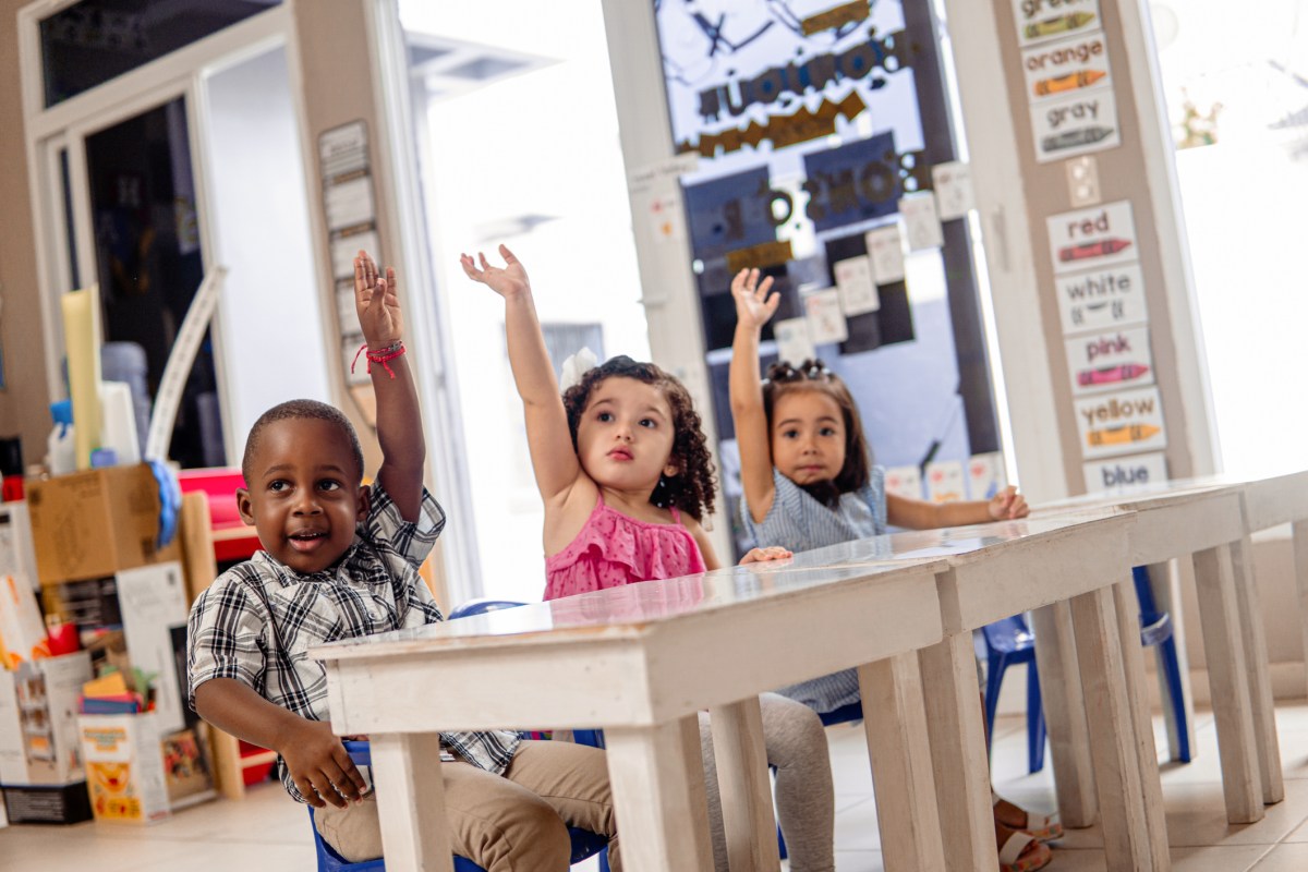 Three little children with your hands up in a class.