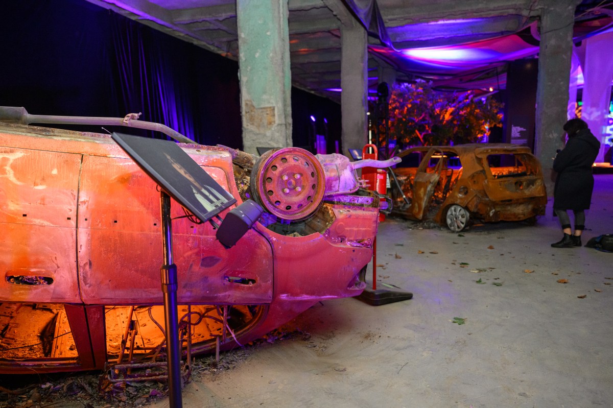 a woman looks at destroyed cars at the Nova Music Festival exhibit in NYC