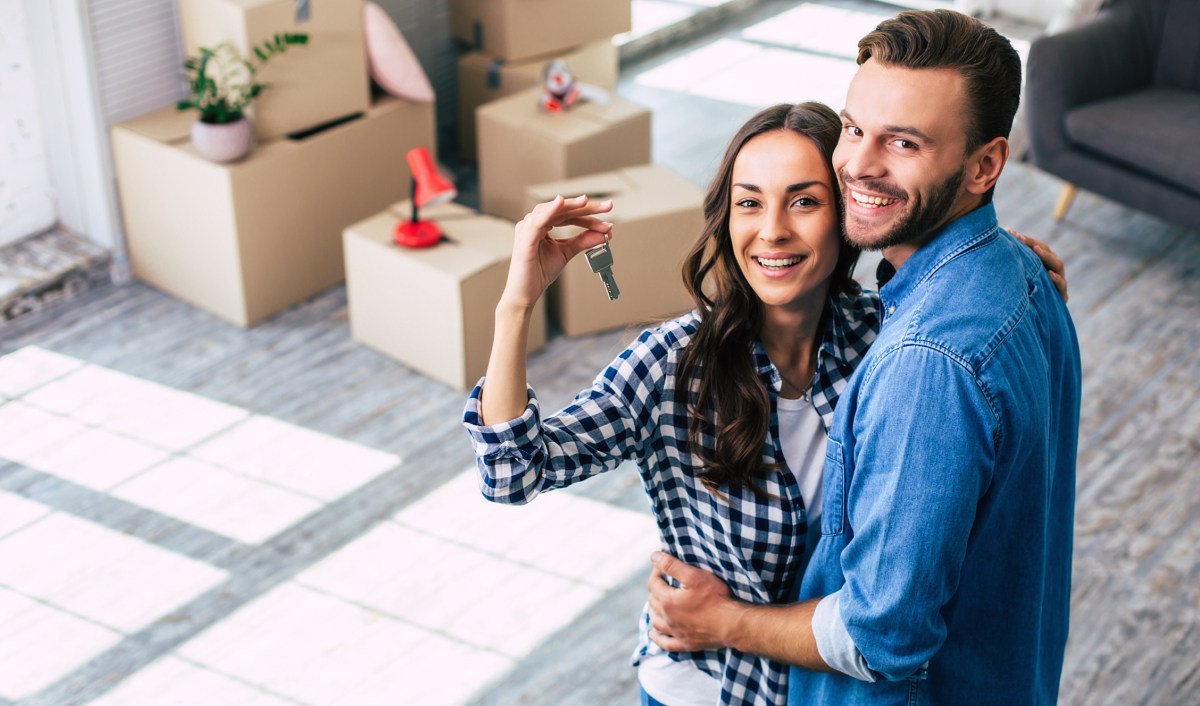 Happy housewarming. A young couple holds happily a key to their new home which they were so excited about, and this can't but make them feel overwhelmed with positive emotions.