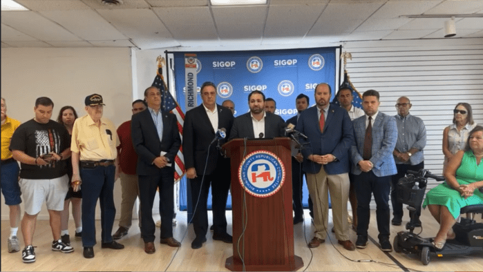 group of men and women inside a building at a podium speaking about attempted assassination of Donald Trump