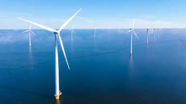 Windmill park in the ocean, drone aerial view of windmill turbines generating green energy electrically, windmills isolated at sea in the Netherlands with a blue sky at summer