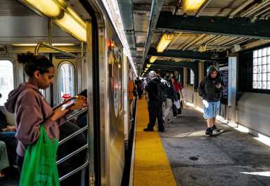 Commuters on board a stopped 7 train and walking on a platform in Queens on Oct. 22, 2024.