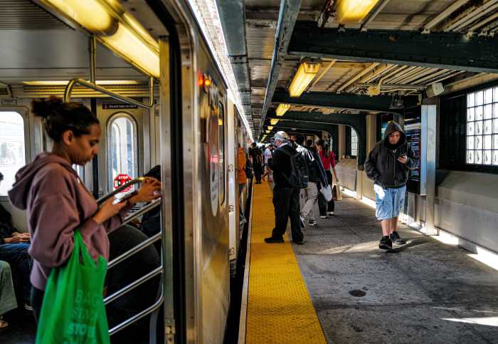 Commuters on board a stopped 7 train and walking on a platform in Queens on Oct. 22, 2024.