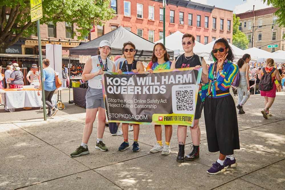 5 people standing and holding a KOSA Banner