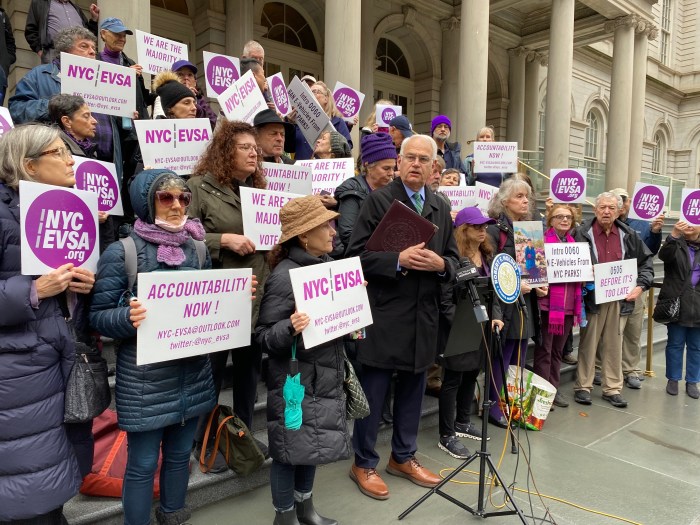 Pushing back: Why immigrant and hospitality advocacy groups are fighting NYC e-bike registration bill 3 people on steps with signs supporting registration for an e-bike licensing bill in NYC