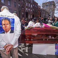 COVID memorial in Brooklyn with casket and guy wearing shirt with photo of Andrew Cuomo
