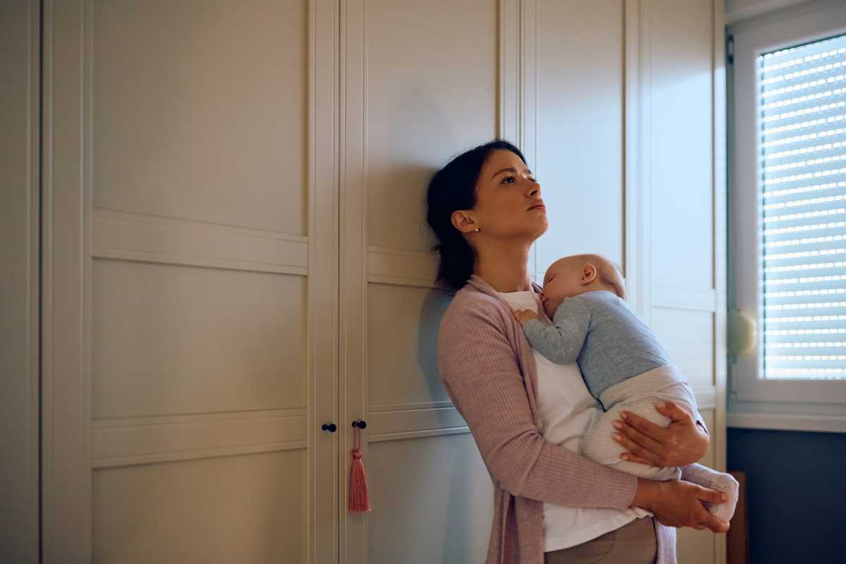 Distraught mother thinking of something while her baby is napping in her arms. Copy space.
