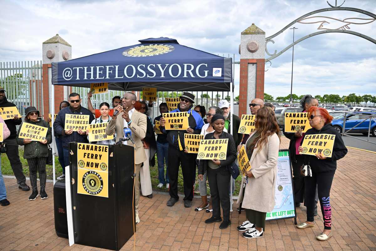 a group of people in Brooklyn behind a podium holding signs that read Canarsie ferry now