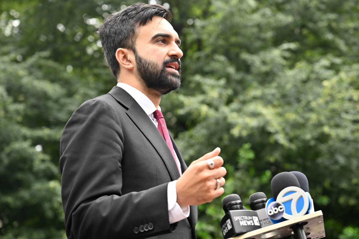 man with beard and suit speaking at podium with microphones