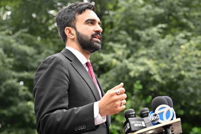 man with beard and suit speaking at podium with microphones