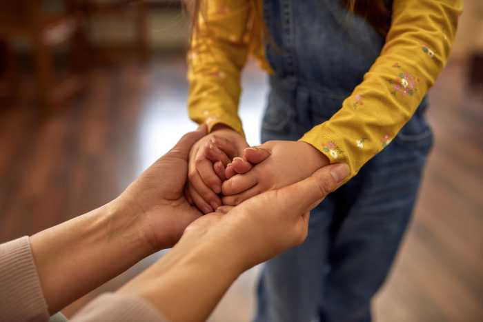 Unrecognisable female hands holding tight little child's hands. Foster parent created supportive and safe environment for adopted child. Taking care emotionally concept.
