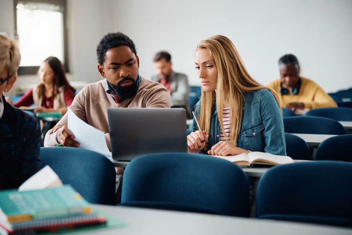 Multiracial students cooperating while e-learning on laptop during adult education training course in the classroom.