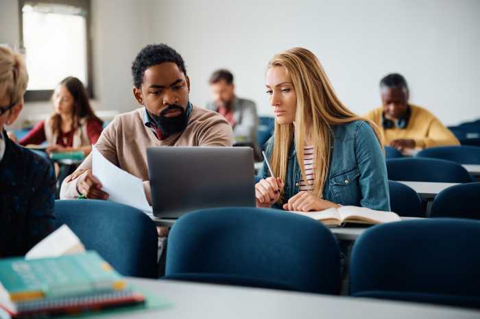 Multiracial students cooperating while e-learning on laptop during adult education training course in the classroom.