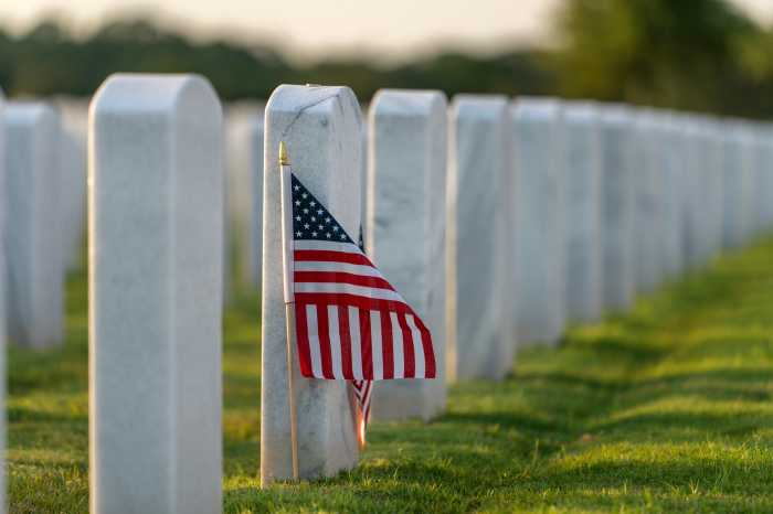 Military burial headstones. Sarasota National Cemetery with rows of white tomb stones and USA flags on green grass. Memorial Day concept.