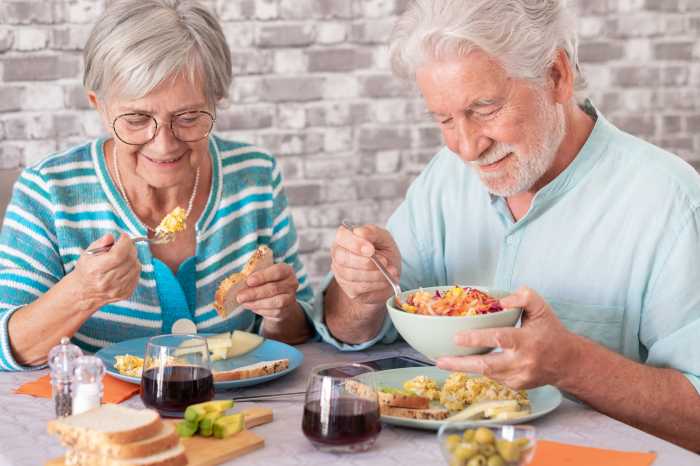 Smling carefree caucasian senior couple sitting at table having a brunch together at home enjoying an healthy eating together
