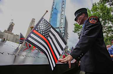firefighter mourns at 9/11 memorial with black and white american flag with red stripe