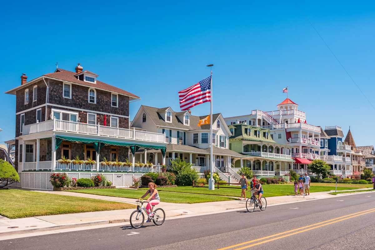 People bike and walk in front of traditional villas in Cape May, NJ, on a sunny summer day on the Jersey Shore