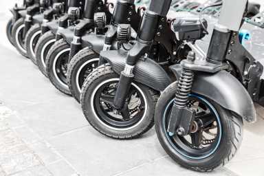Scooters parked neatly in a row on a city sidewalk. Row of black rental electric scooters lined up on a street
