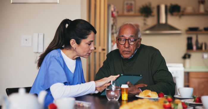 Tablet, conversation and nurse with senior man at assisted living for diagnosis explanation. Digital technology, healthcare and caregiver with elderly patient for medical checkup in retirement home