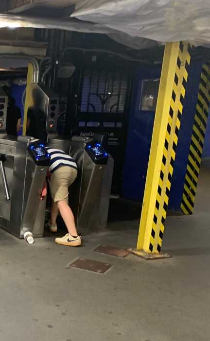 person ducking under a turnstile in a subway station