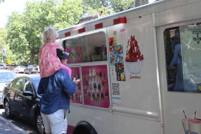a child sits on her dad's shoulders while buying ice cream from an ice cream truck during a NYC heat wave