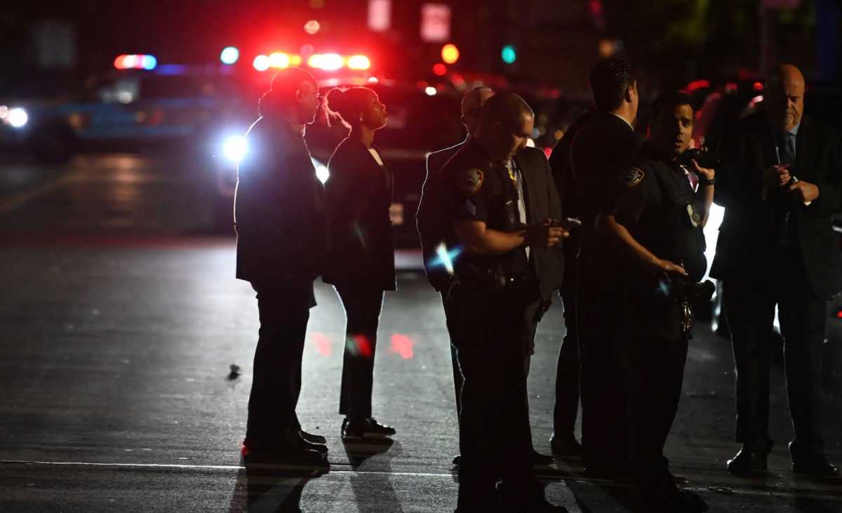 police officers and detectives people standing around at ngiht with police car warning lights glowing in background