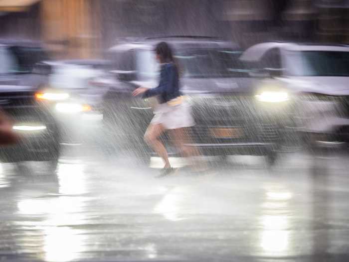 Person running into rain-soaked street in New York City amid flooding rain