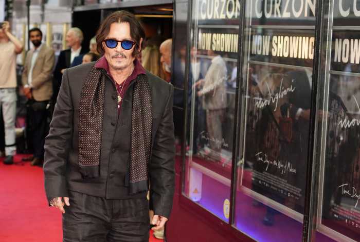 man with sunglasses, long hair and coat on red carpet.