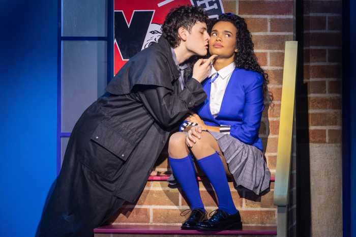 guy in black trench coat kisses woman in purple blazer and socks in broadway production