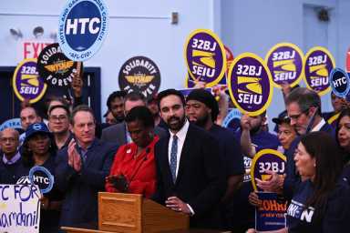 People holding purple union signs behind man in black suit at podium