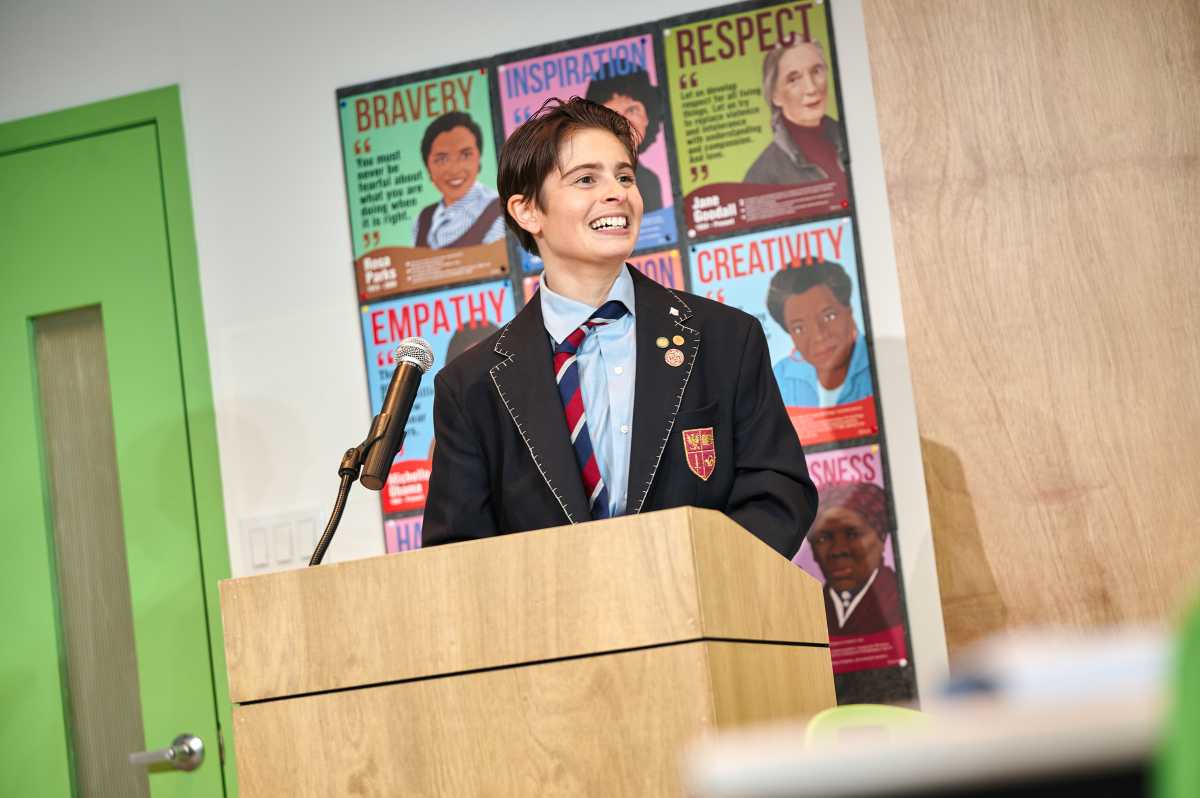 woman in boys school uniform standing at podium during debate in Trophy Boys