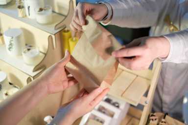 unrecognizable woman vendor at a colorful market exchanges a paper bag of purchases with a customer, emphasizing the growing role of female entrepreneurs in the business landscape
