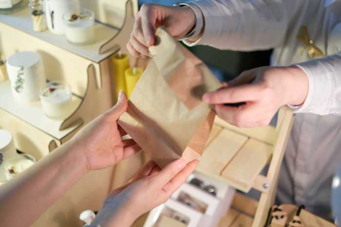 unrecognizable woman vendor at a colorful market exchanges a paper bag of purchases with a customer, emphasizing the growing role of female entrepreneurs in the business landscape
