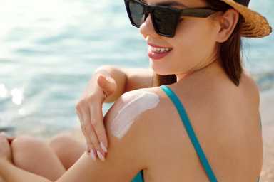 Woman putting sunblock lotion on shoulder before tanning during summer holiday on beach. Sun cream. Suntan. Beautiful Woman Applying Sunscreen Solar