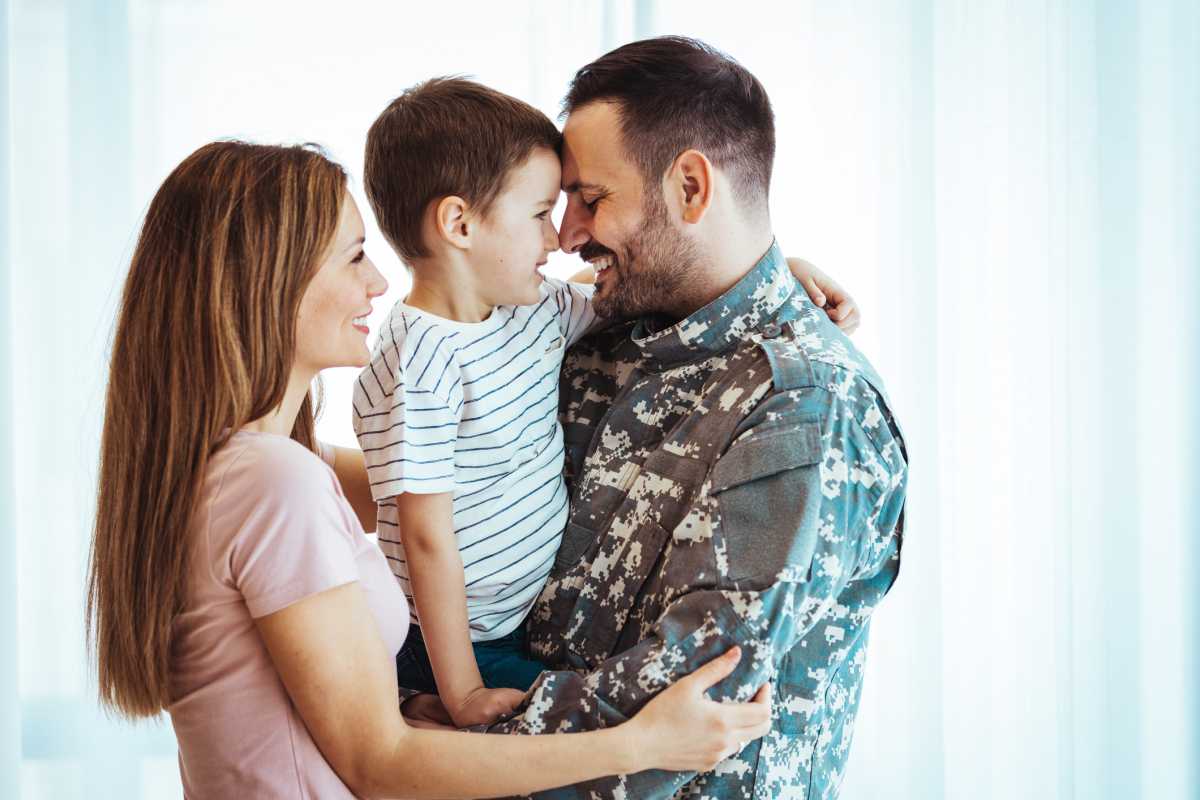 A Caucasian mother and father lovingly embrace their young son, sharing a tender moment together in a well-lit room with sheer curtains.