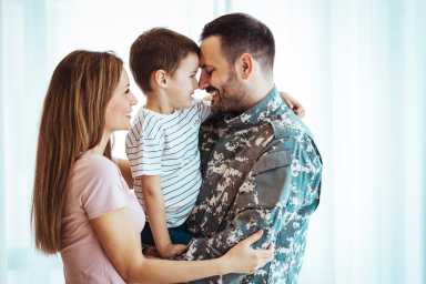 A Caucasian mother and father lovingly embrace their young son, sharing a tender moment together in a well-lit room with sheer curtains.