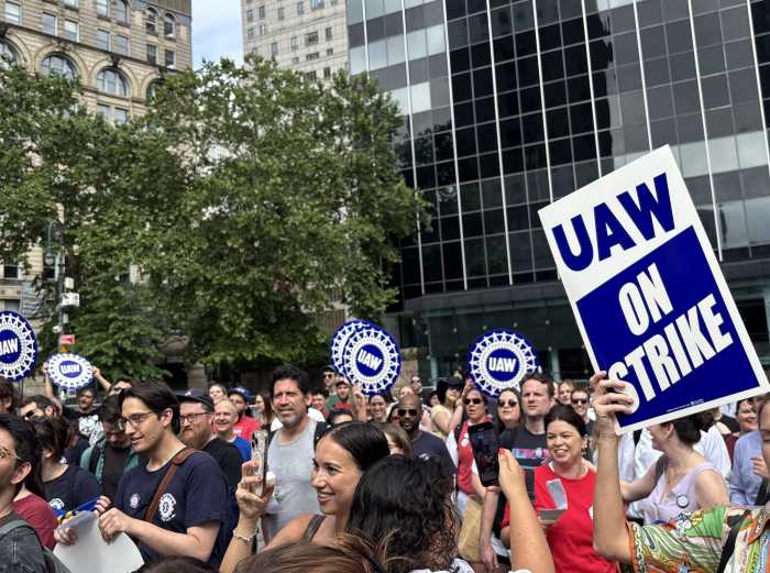 Unionized public interest attorneys in NYC holding banners during a strike for better wages, lower caseloads, and retirement benefits.