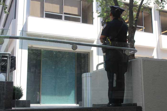 An NYPD officer secures the scene outside 345 Park Ave. as shattered glass from the lobby windows reflects the violence that left four dead Monday evening.