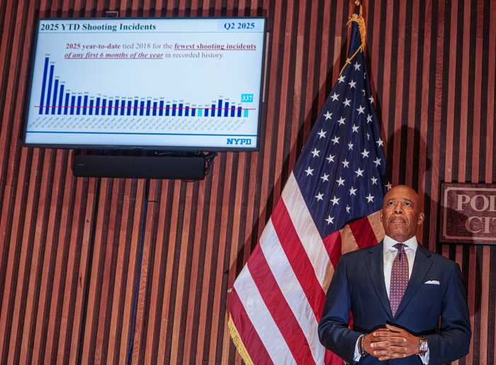 man in suit standing in front of American flag next to bar chart on screen above