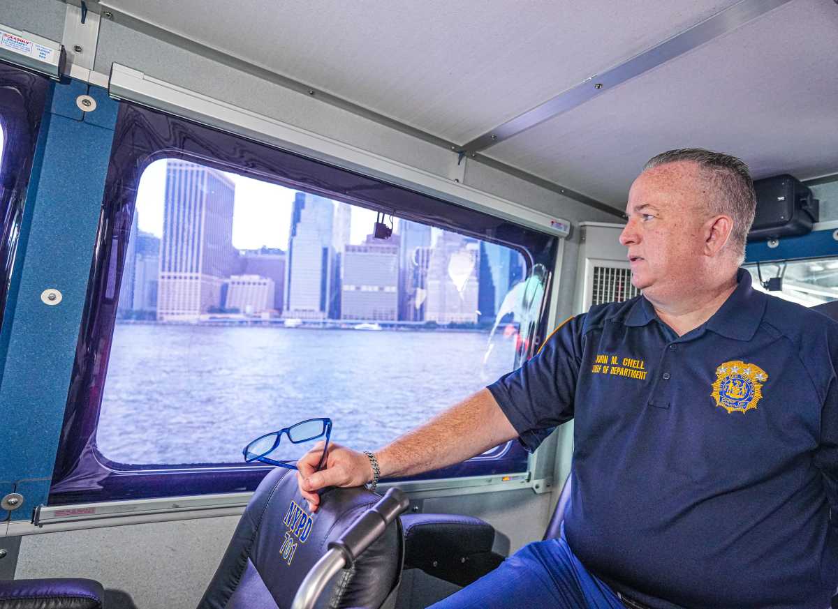Man in NYPD shirt at the helm of boat in New York Harbor