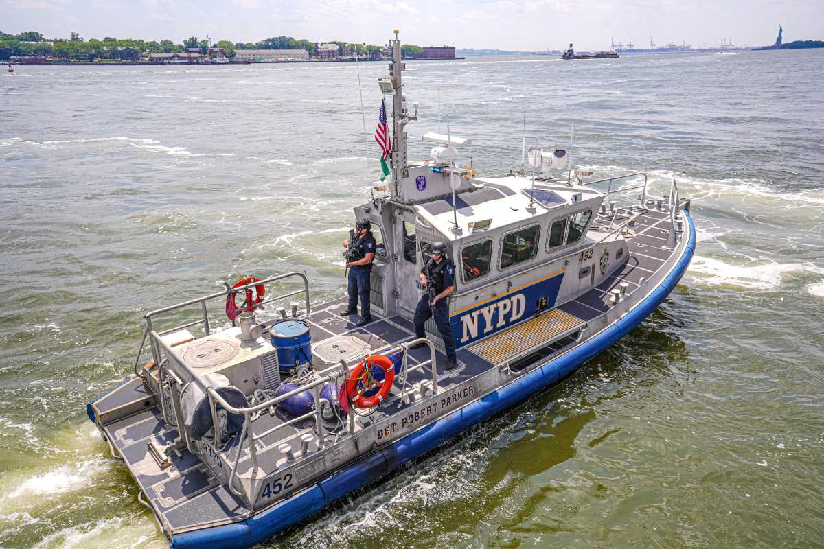 Police boat with NYPD logo riding in murky green water of East River
