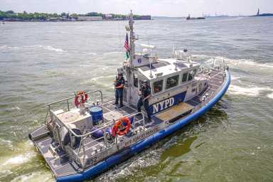 Police boat with NYPD logo riding in murky green water of East River