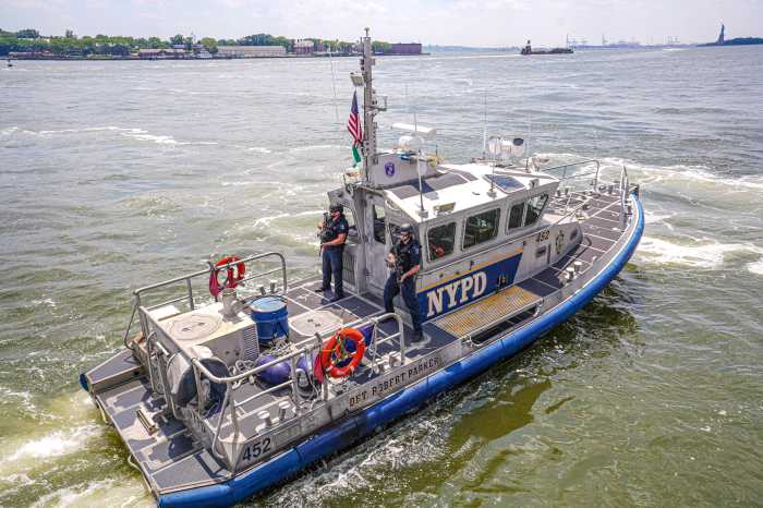 Police boat with NYPD logo riding in murky green water of East River