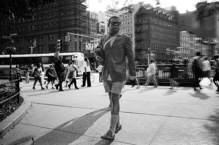 A man in shorts striding along a New York City sidewalk during summer in black and white