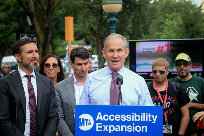 man wearing a purple tie at a podium flanked by a group of people
